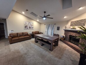 Un salon avec un canapé en cuir marron, une table basse en bois, une cheminée et un ventilateur de plafond.