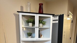 Een kleine keuken met een wit kastje, een zwarte koelkast en een prullenbak.