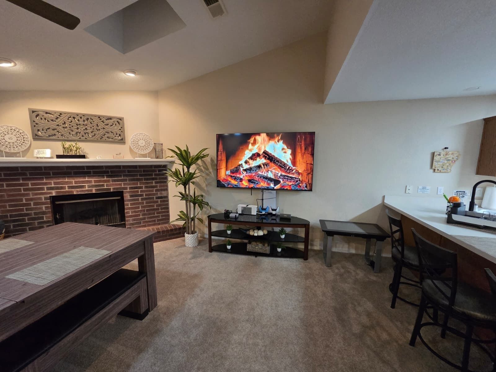 A living room with a fireplace, a TV mounted on the wall, a dining table, and a bar area.
