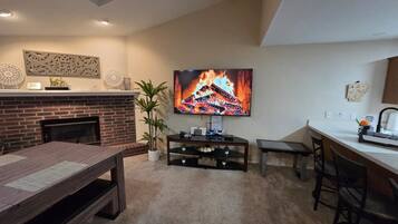 A living room with a fireplace, a TV mounted on the wall, a dining table, and a bar area.