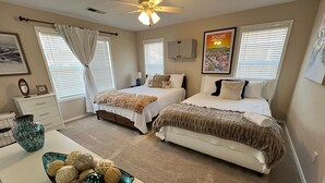 Een slaapkamer met twee bedden, een plafondventilator, een dressoir, een vaas en een schaal decoratieve voorwerpen.