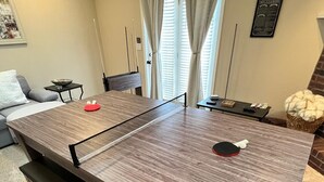 Een tafeltennistafel in een woonkamer met een bank, een bijzettafeltje en een mand.
