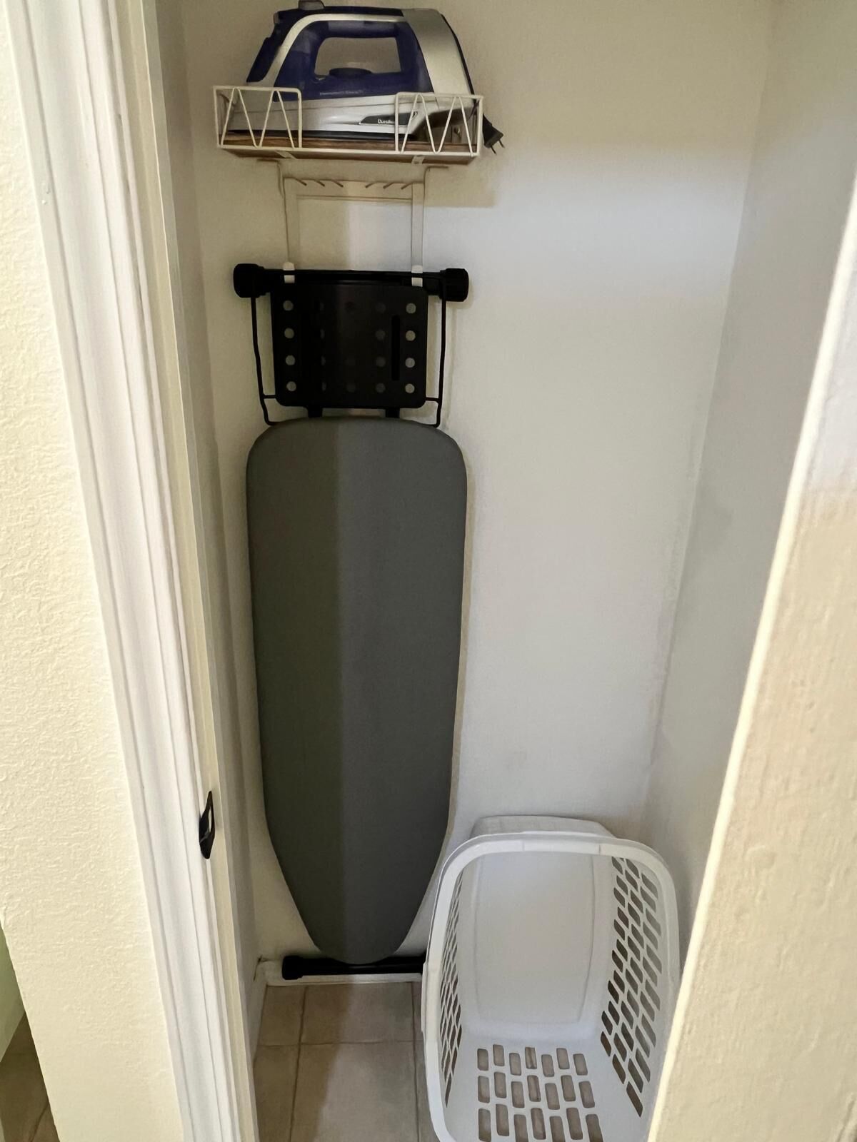 A compact laundry room with a wall-mounted iron, a drying rack, and a laundry basket.