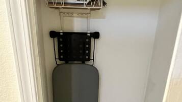 A compact laundry room with a wall-mounted iron, a drying rack, and a laundry basket.