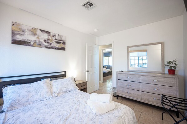 A bedroom with a bed, a dresser, a mirror, and a door leading to another room.