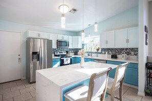 A modern kitchen with white cabinets, stainless steel appliances, a central island with bar stools, and pendant lighting.
