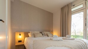 Un lit bien fait, avec une couette blanche, des oreillers et une serviette enroulée posée sur le côté.