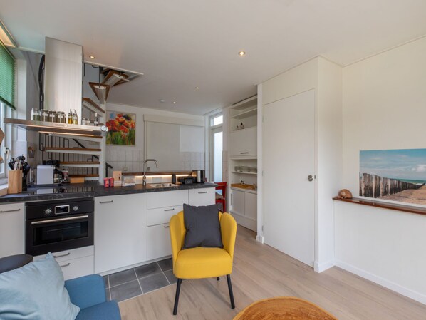 A modern kitchen with white cabinetry, a built-in oven, and a yellow chair.