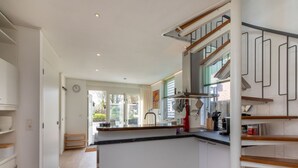 A modern kitchen with a central island, wooden flooring, and a staircase with metal railings.