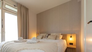 Une chambre moderne avec un grand lit, une literie de couleur beige et une lampe de chevet.