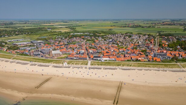 Une vue aérienne d’une ville côtière, avec une plage, des maisons aux toits orange et une église.