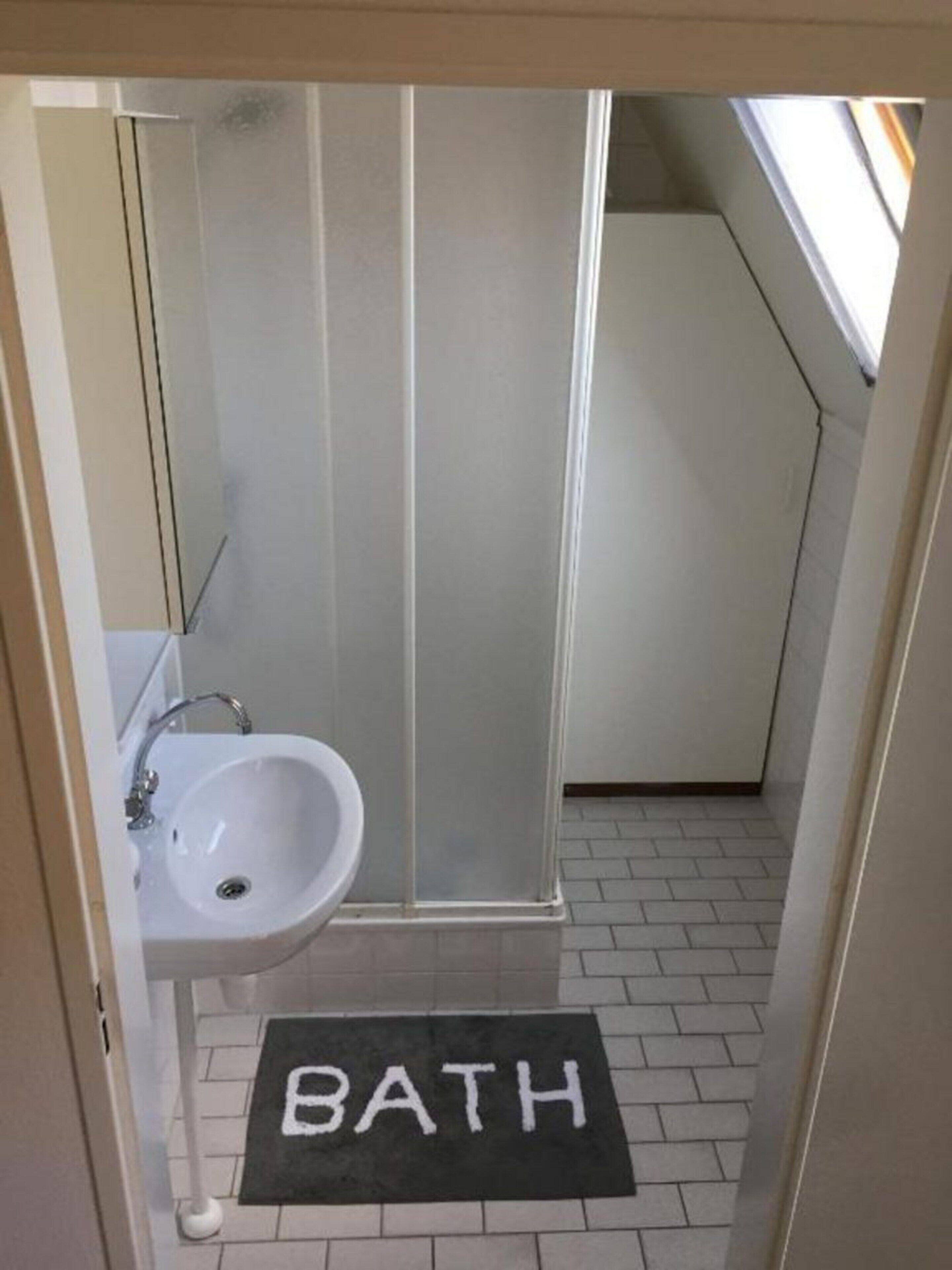 Ein Badezimmer mit Waschbecken, Dusche und einer schwarzen Matte mit dem Schriftzug 'BATH'.