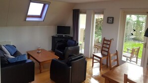A living room with a sofa, a coffee table, a TV, and a balcony with chairs. - Pretty Holiday Home in Burgerburg (Burgerbrug)