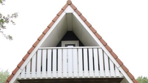 A two-story house with a sloped roof, a balcony with white railings, and a front door with glass panels. - Pretty Holiday Home in Burgerburg (Burgerbrug)