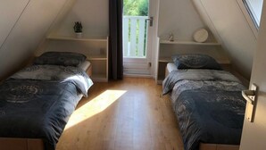 A small attic bedroom with two beds, a window with a view of greenery, and a door leading outside. - Pretty Holiday Home in Burgerburg (Burgerbrug)