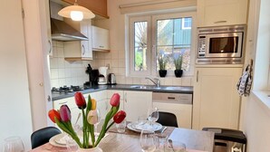 Un coin repas avec une table en bois dressée pour quatre personnes, un vase de tulipes et, au fond, une cuisine moderne.