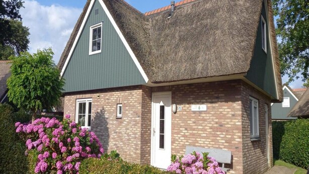 Une maison à deux étages, dotée d’un toit à forte pente, d’une façade en briques et d’un petit porche à l’avant avec un banc.