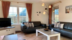 Un salon moderne avec deux canapés en cuir noir, une table basse en bois, un téléviseur posé sur un meuble et un coin repas avec une table et des chaises.