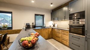 Eine moderne Küche mit Holzschränken, einem Edelstahlbackofen und einer Obstschale auf der Arbeitsplatte.