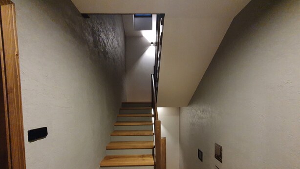 Ein schmaler Korridor mit einer Holztreppe, die zu einer Zwischenebene führt.