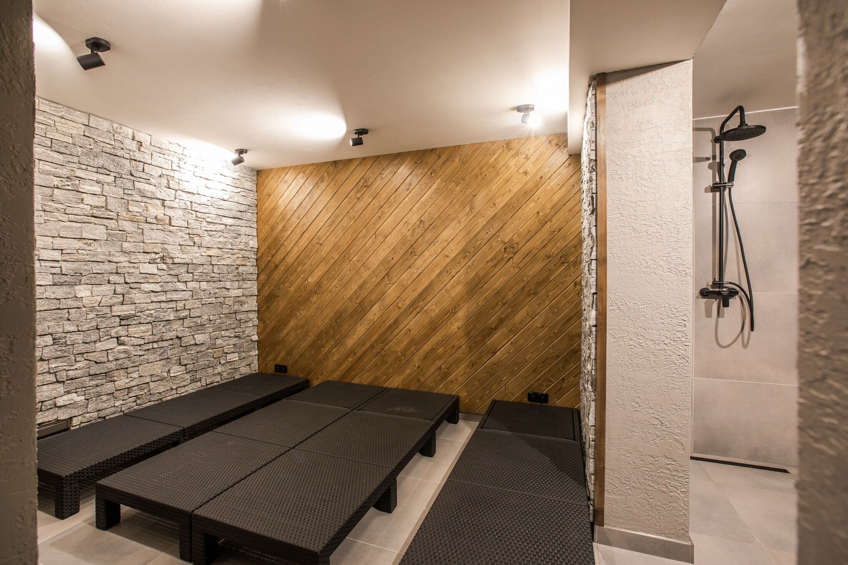 Ein Wellnessbereich mit Stein- und Holzvertäfelung, Bänken und einer Dusche.