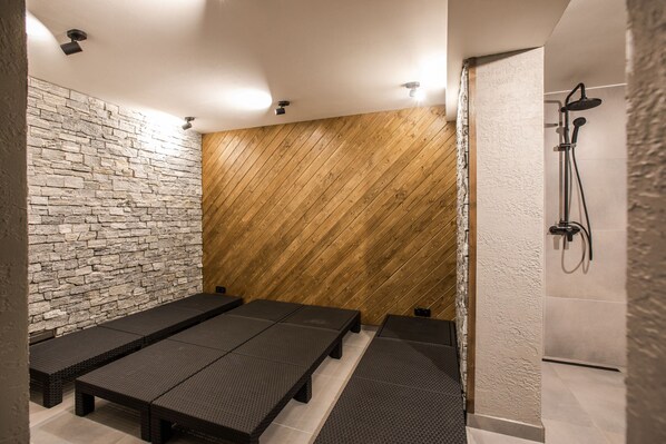 A spa area with stone and wooden walls, benches, and a shower.