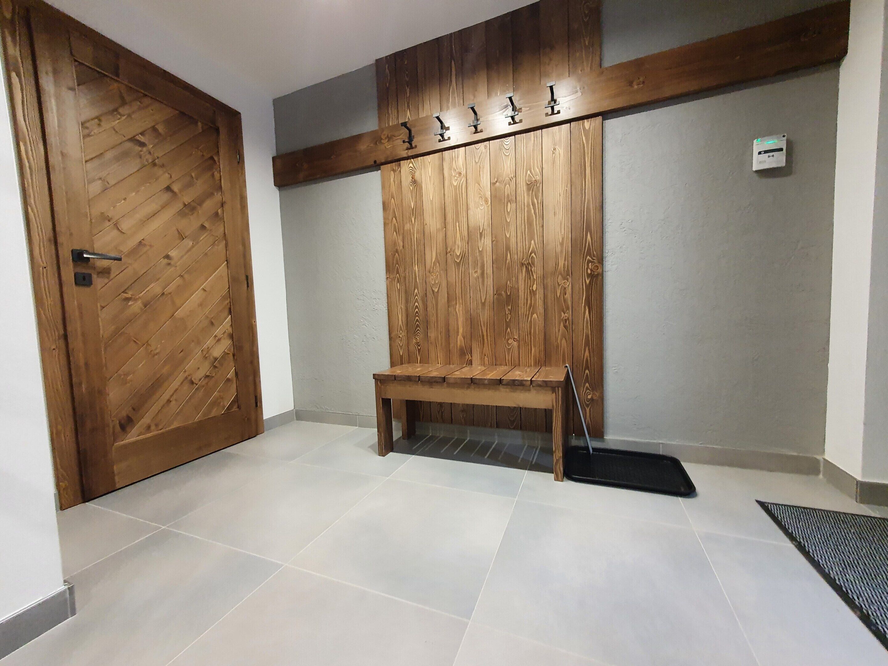 Un pasillo con una puerta de madera, un banco y un perchero en la pared.