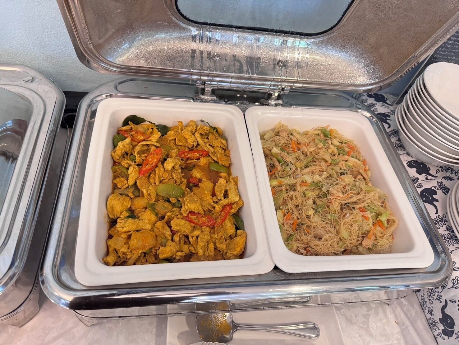Two food containers with various dishes, a stack of plates, and a spoon.