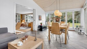 A modern living room with a dining area, large windows, and a wooden ceiling.