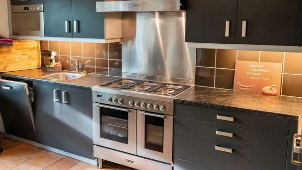 A modern kitchen with dark cabinetry, stainless steel appliances, and a tiled backsplash. - Furnished Bungalow With Garden (Sint Maartensvlotbrug)