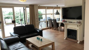 A living room with a black leather sofa, a wooden coffee table, a TV, and a fireplace. - Furnished Bungalow With Garden (Sint Maartensvlotbrug)