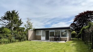 Ein modernes eingeschossiges Haus mit überdachter Terrasse, Rasen und Garten.