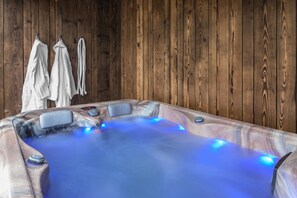 A hot tub with blue LED lights, wooden walls, and towels hanging on hooks.