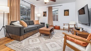 A modern living room with a sofa, coffee table, and chairs, a ceiling fan, and a large window with curtains. - Charming 3-bedroom house near downtown Boise with AC, WiFi (Boise)