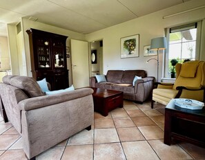 A living room with a brown sofa, a brown armchair, and a yellow armchair. There is a wooden cabinet and a lamp on a table. - Holiday Home in Sint Maartenszee for 6 (Sint Maartensvlotbrug)