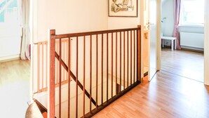 Eine Treppe mit hölzernem Geländer führt zu einer oberen Etage. Ein gerahmtes Bild hängt an der Wand darüber.