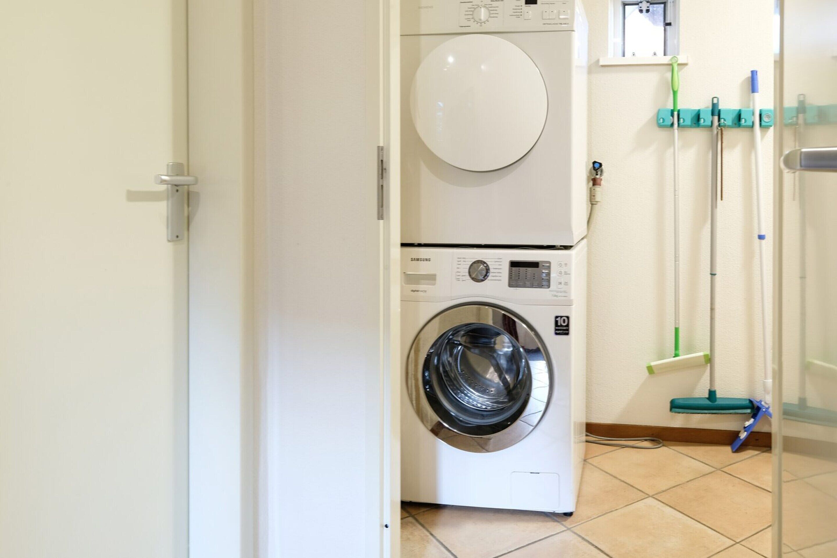 A laundry area with a stacked washer and dryer, a mop, and a broom.