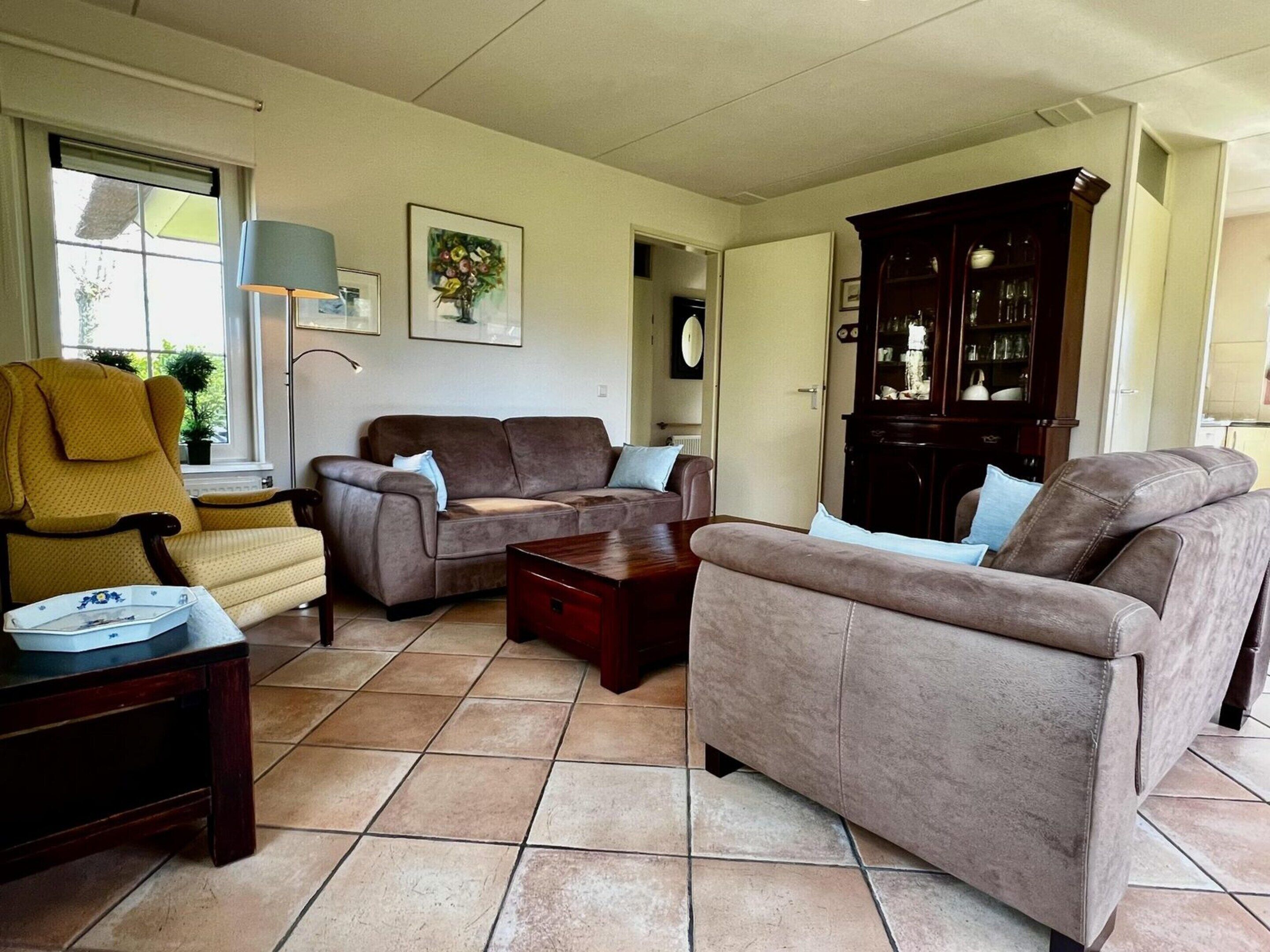 A living room with a brown sofa, yellow armchair, and a dark wooden cabinet.
