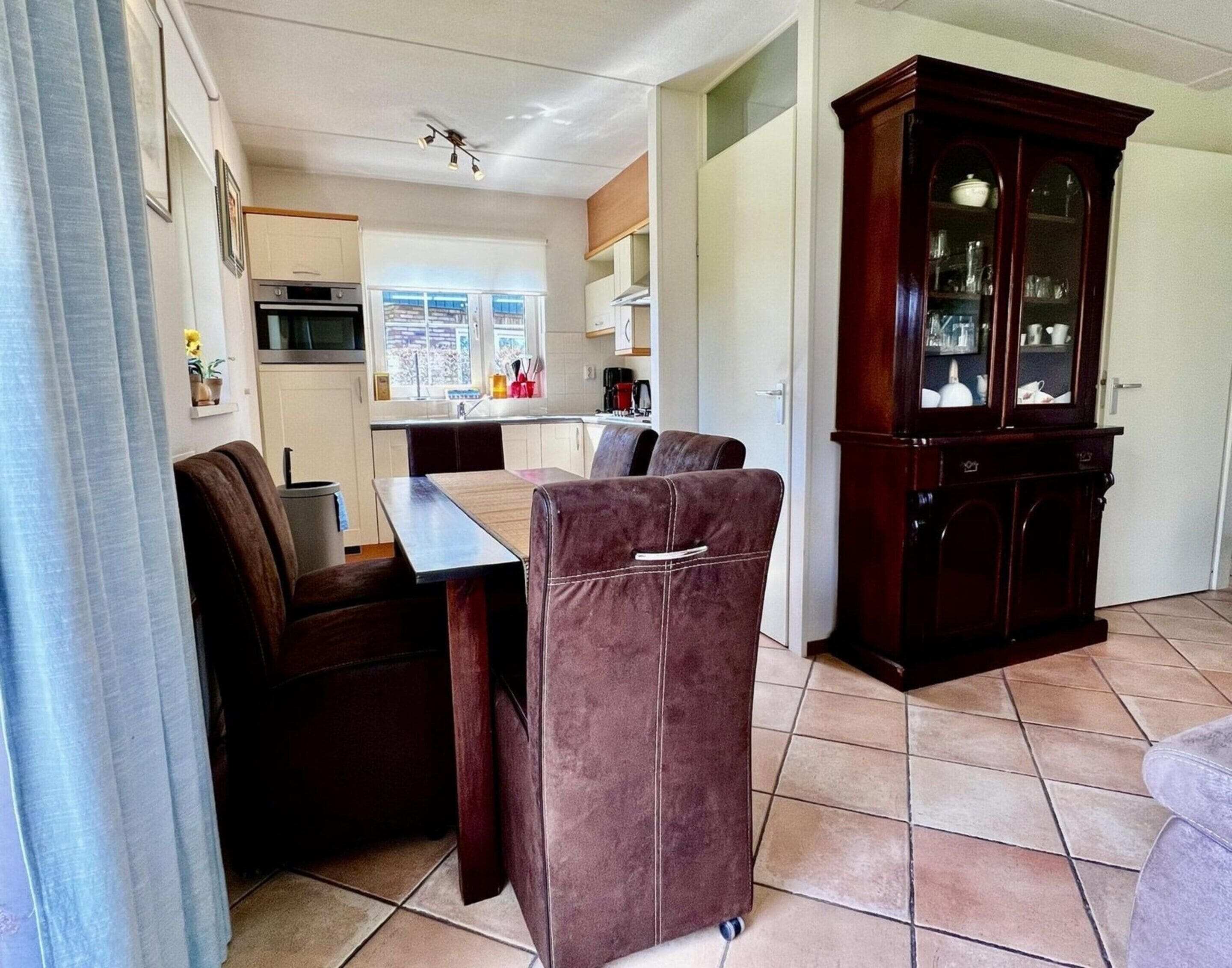 A compact living space with a kitchenette, a dining area with a table and chairs, and a large wooden cabinet.