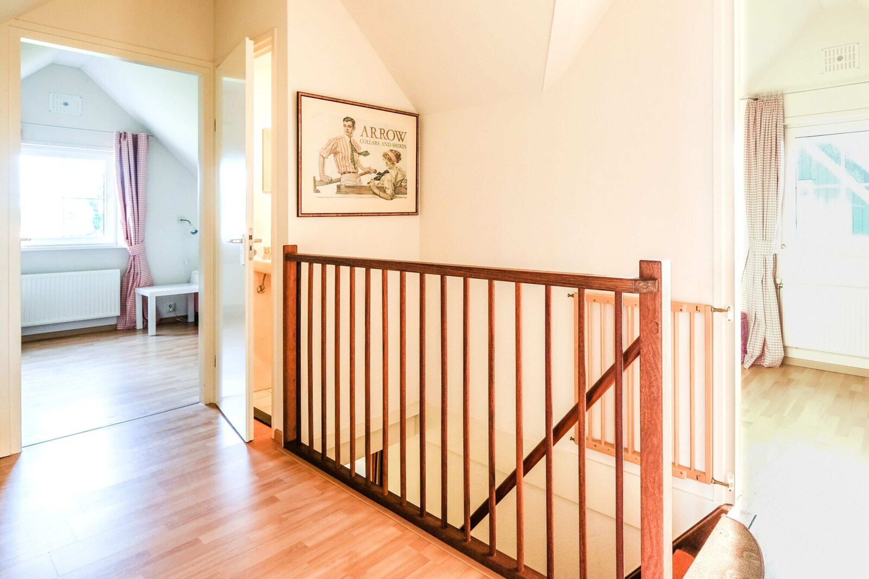 Un corridoio con pavimento in legno, una scala con ringhiera in legno e un quadro appeso al muro.