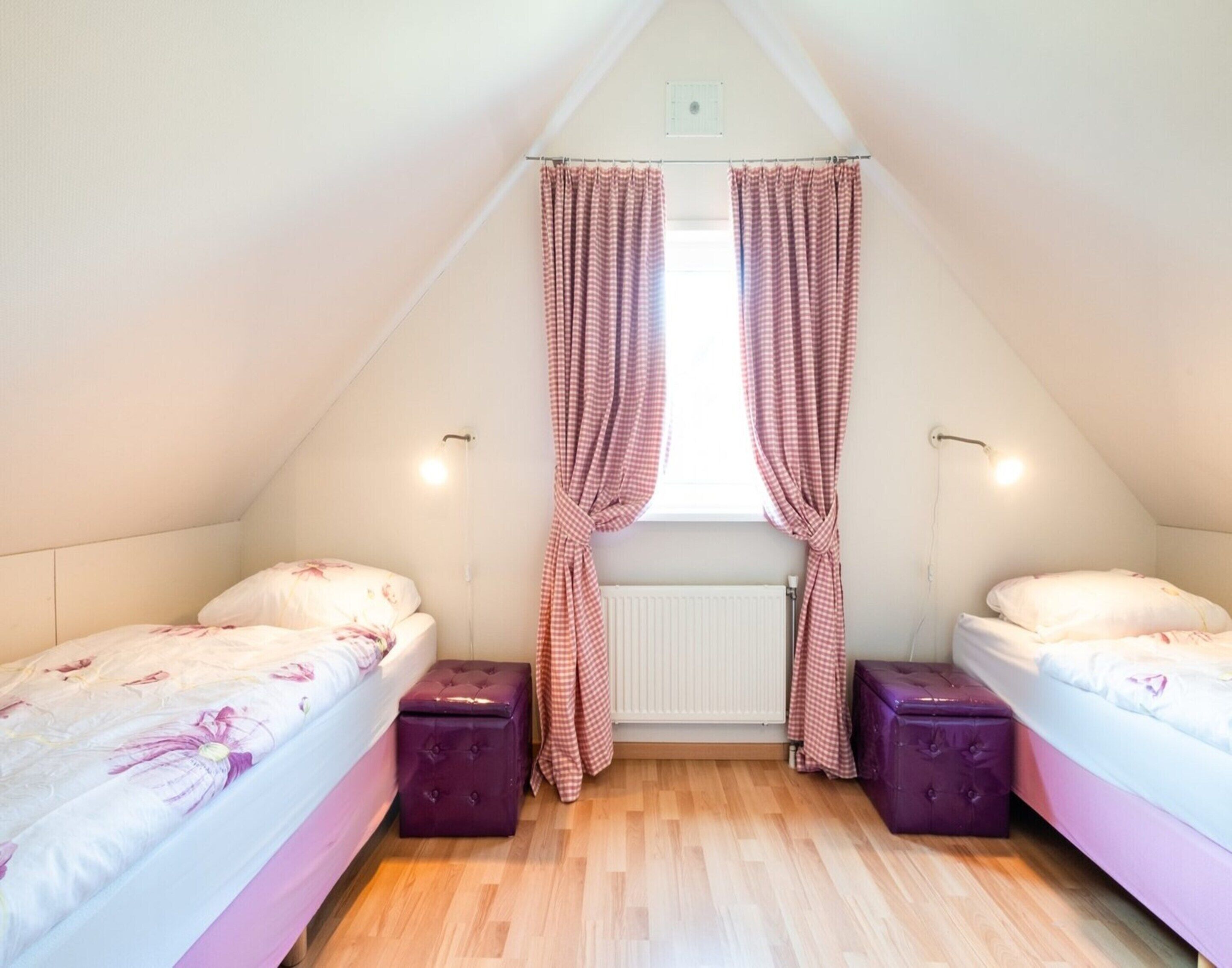 Ein kleines, dreieckiges Schlafzimmer im Dachgeschoss mit zwei Betten, einem Heizkörper und karierten Vorhängen.