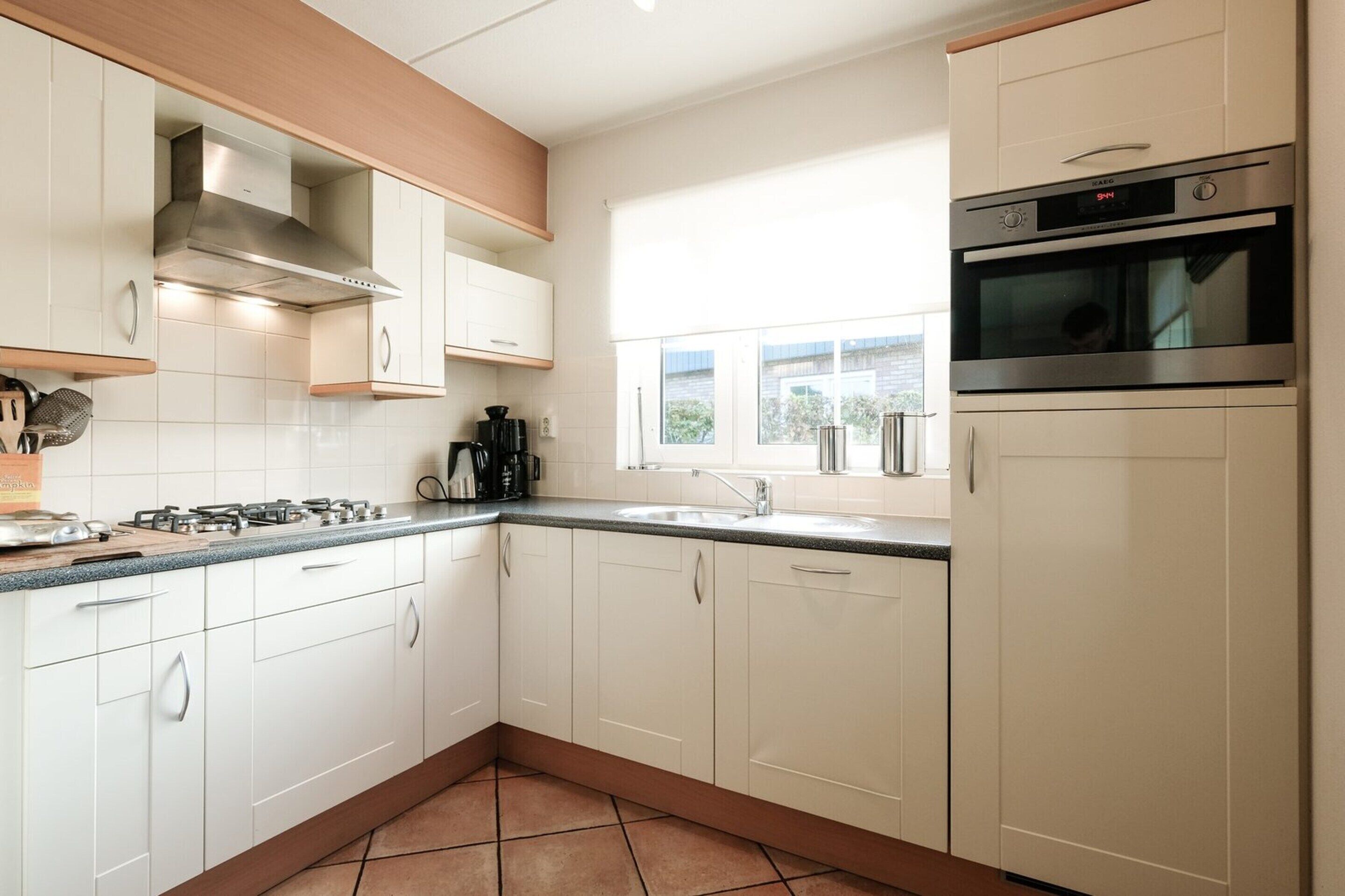 A modern kitchen with white cabinets, a stainless steel range hood, a built-in oven, and a window providing natural light.