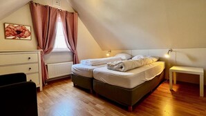 Ein gemütliches Schlafzimmer im Dachgeschoss mit schrägen Wänden, einem Bett mit zwei Kissen, einem Nachttisch, einer Heizung und einem Fenster mit karierten Vorhängen.