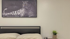 Een slaapkamer met een bed, kussens, een nachtkastje met een plantje, en een lijst met een foto aan de muur.