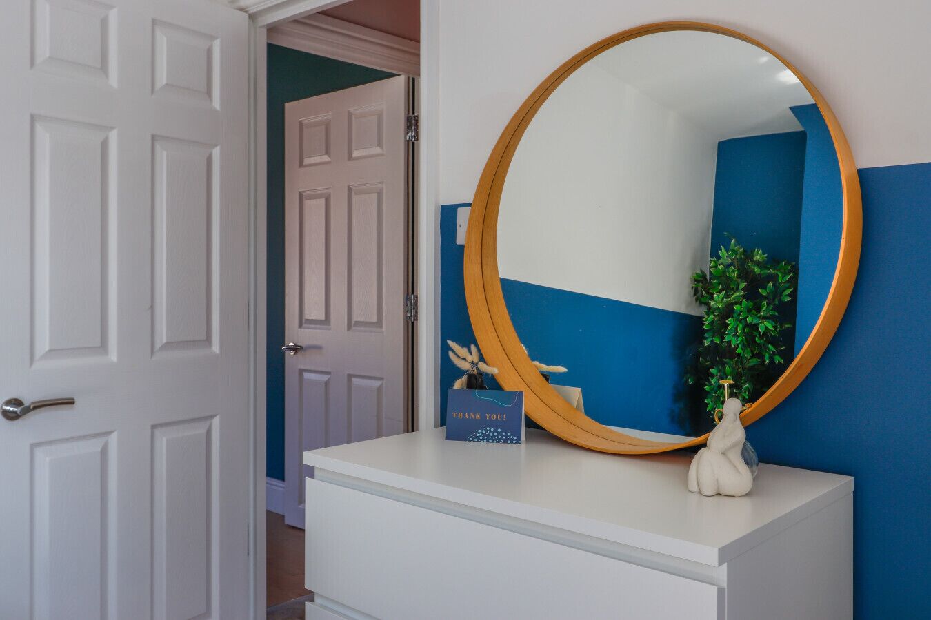 Een witte dressoir met een ronde spiegel en een bedankkaartje.