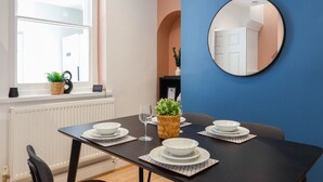 A dining area with a black table set for four, white plates, a wine glass, and potted plants.