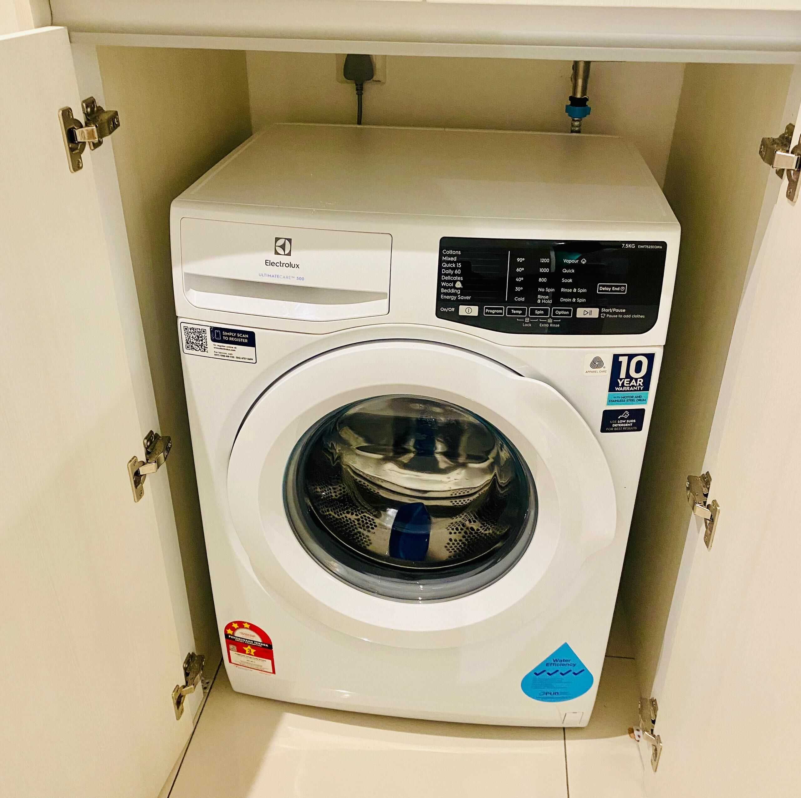Une machine à laver Electrolux blanche, avec un autocollant indiquant une garantie de 10 ans, placée sous un meuble.