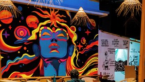 A cafe interior with a colorful mural, hanging lights, and a counter with the name 'Simple Belle Cafe'. - Half Orange (Vagator)