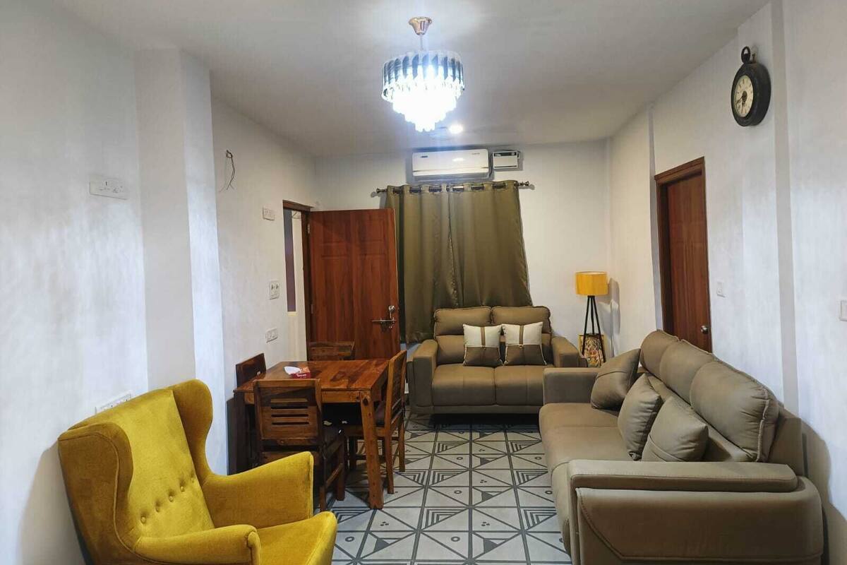A living room with a sofa, armchairs, a dining table, and a chandelier.