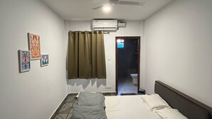 A bedroom with a bed, a ceiling fan, an air conditioner, and a door leading to a bathroom. - Half Orange (Vagator)